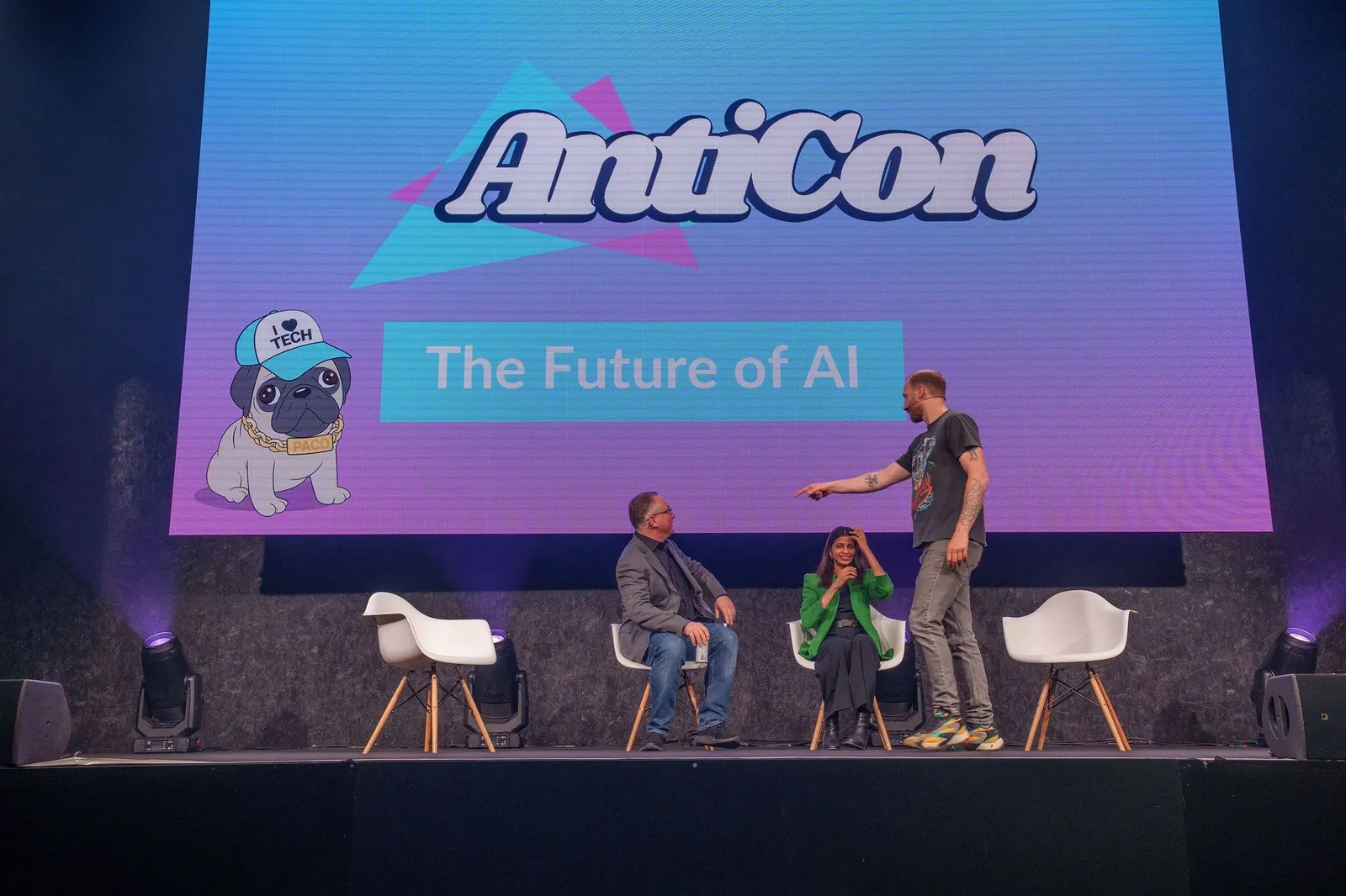 Parry Malm standing on a panel stage at AntiCon, mid-gesture, with two seated panellists beneath a screen reading The Future of AI.